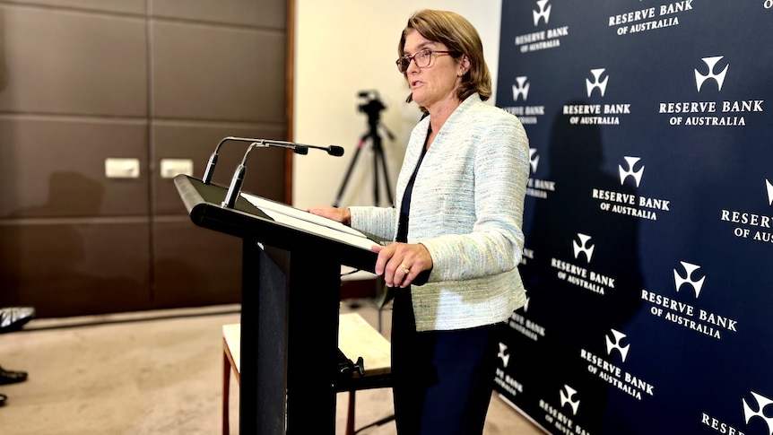 RBA governor Michele Bullock stands at a podium speaking at a press conference.