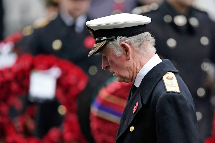 Prince Charles looks down somberly in a memorial service wearing a military uniform