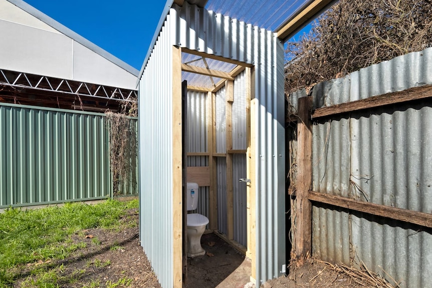 A corrugated iron structure with a toilet inside and clear pyrex roof. 