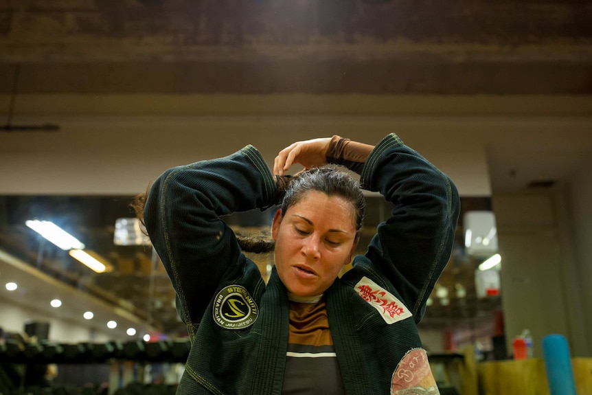 A woman refastening her hair while dressed in a jiu-jitsu uniform.
