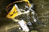 A yellow bike partially submerged in water next to a bluestone wall.