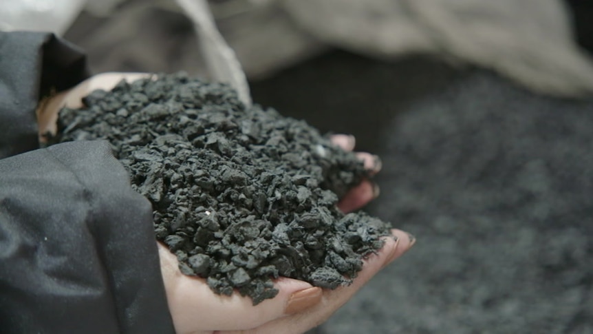 A pair of hands holds black asphalt.