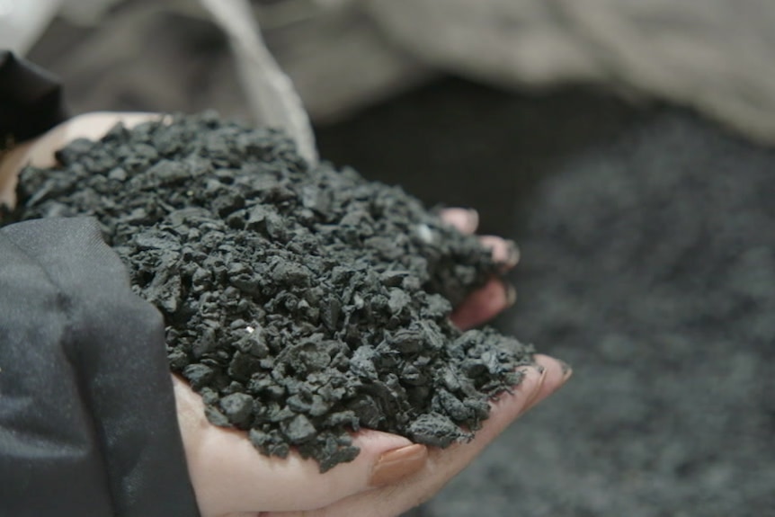 A pair of hands holds black asphalt.