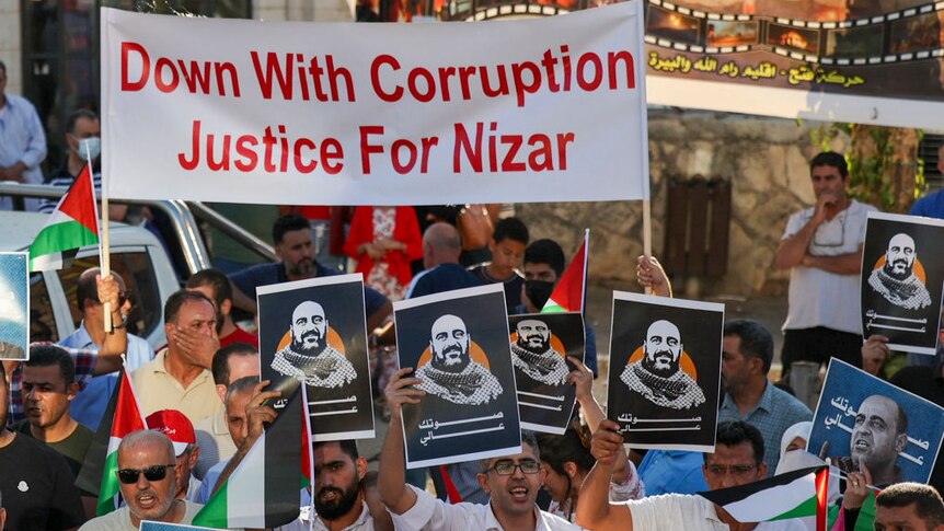 crowd of protestors with print out images of Nizar Banat and large banner reading "down with corruption, justice for Nizar."
