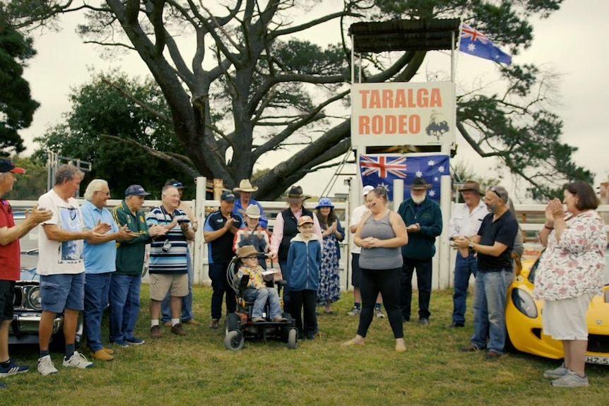 A group of people applaud out the front of a sign saying 'Taralga Rodeo.'