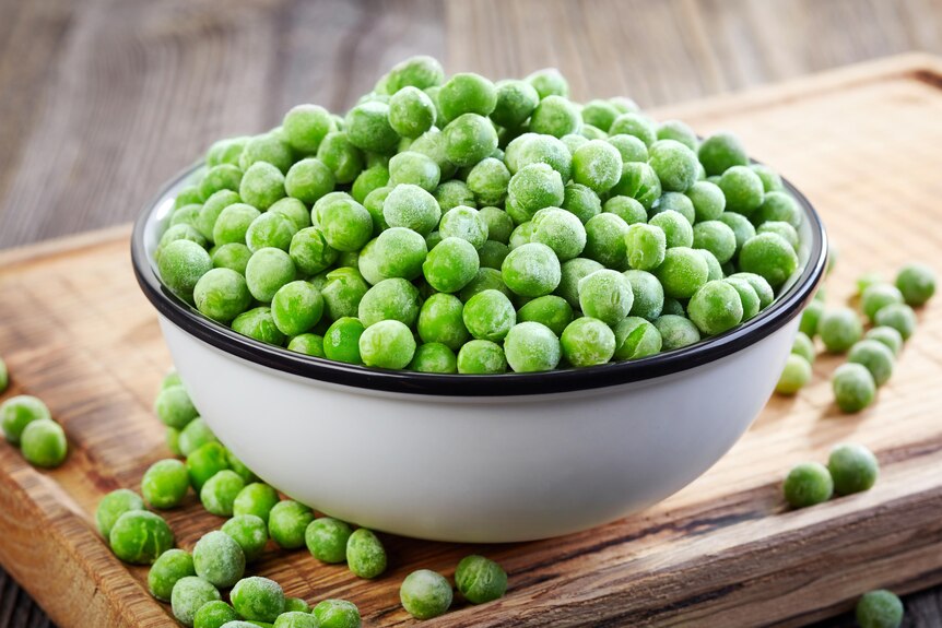 A white china bowl filled with frozen peas