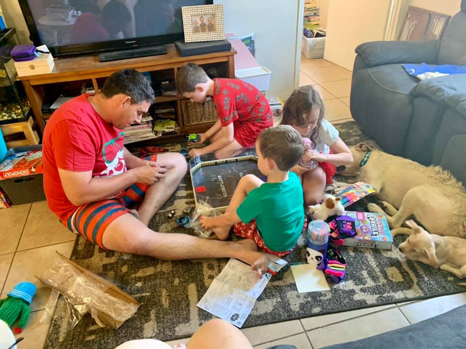 A dad plays with his three children on the floor of a living room
