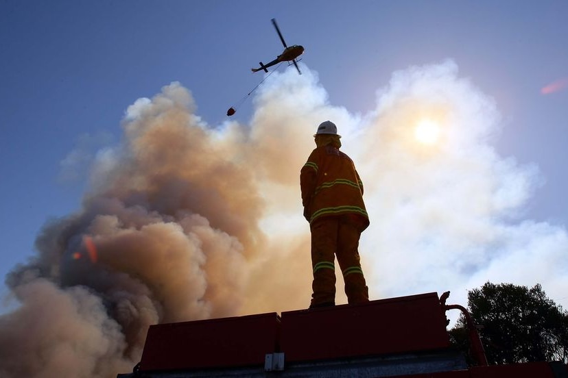 A firefighter watches a helicopter water bomb a bushfire near the town of Peats Ridge