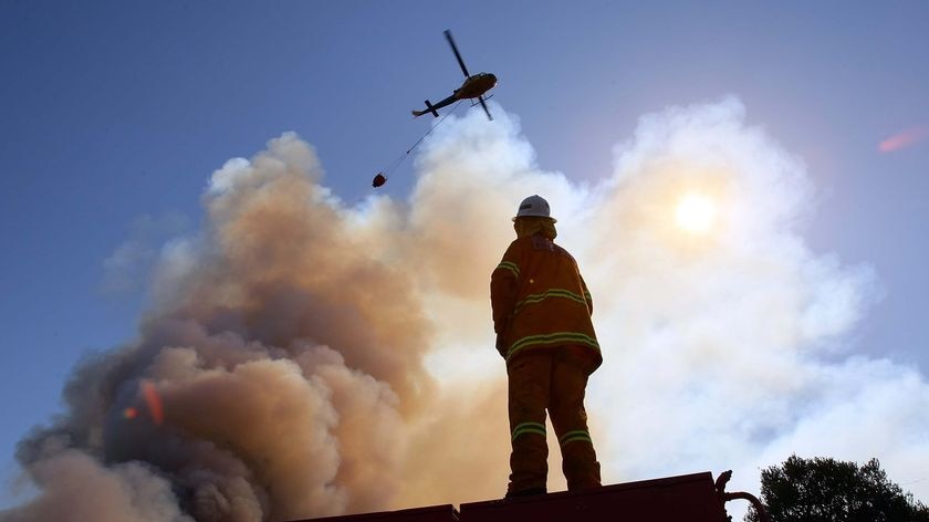 A firefighter watches a helicopter water bomb a bushfire near the town of Peats Ridge