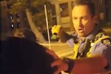 A police officer stands pointing a taser at a man whose face is blurred at night.