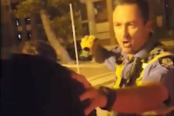 A police officer stands pointing a taser at a man whose face is blurred at night.