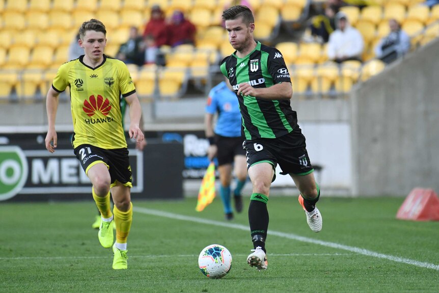 A Western United player dribbles the ball alongside a Wellington Phoenix opponent in the A-League.