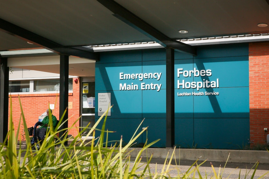 The entry to Forbes hospital with a woman on wheelchair and bush in foreground