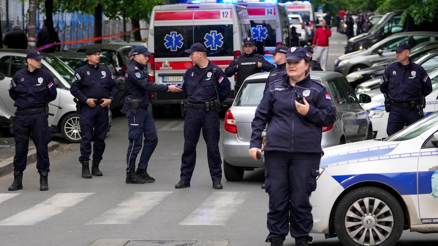 Police standing around a street with several ambulance in the background