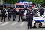 Police standing around a street with several ambulance in the background