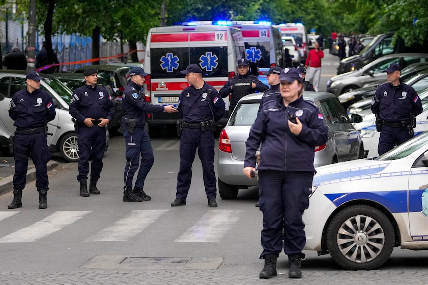 Police standing around a street with several ambulance in the background