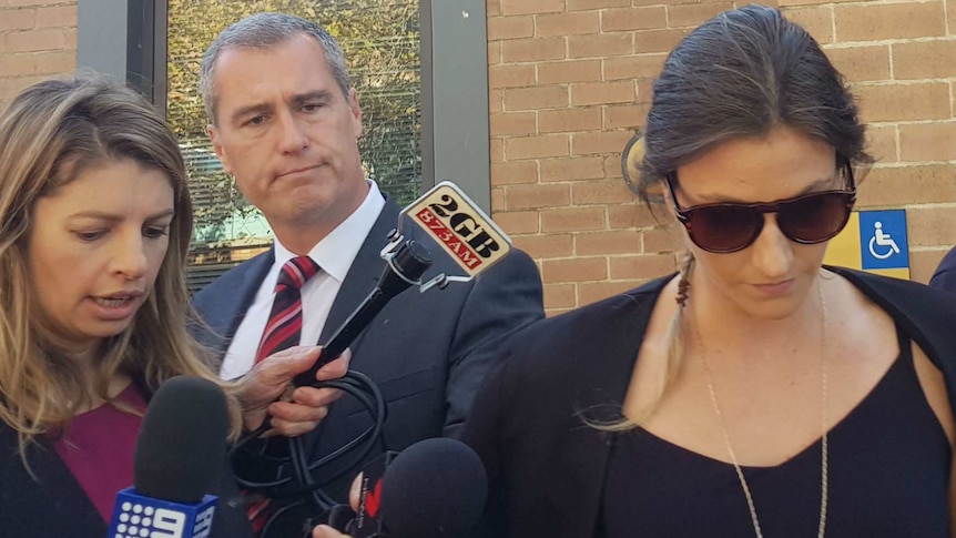 a woman in sunglasses with her head down walks around from a building with television cameras around