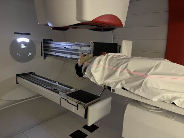A person covered by a blanket as they lay in between two elongated machines with laser lines over their body