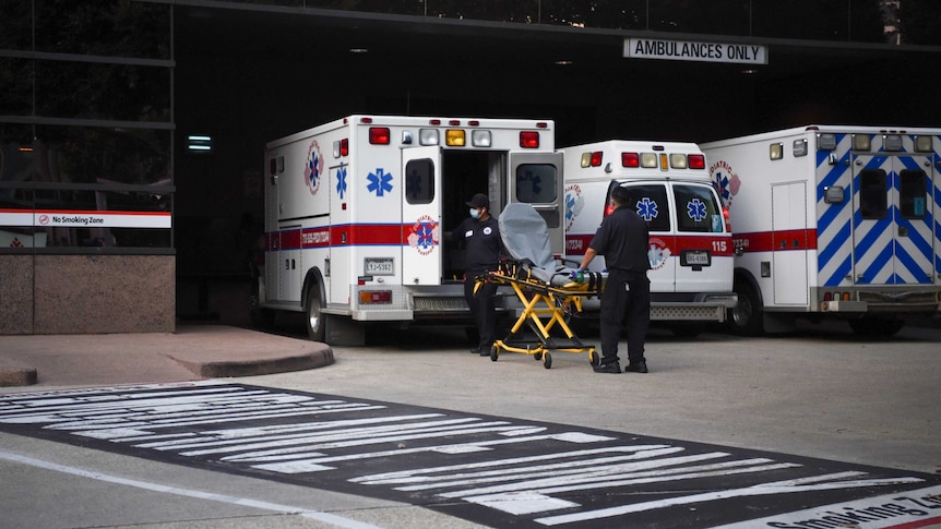 A stretcher is wheeled towards a row of white ambulances by healthcare workers.