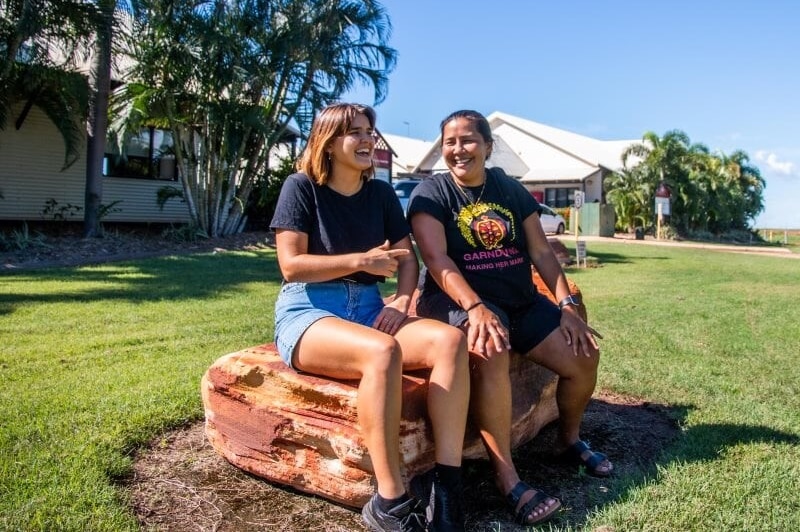 Liv Trounce sits on a rock laughing with her friend Layla Yu, they worth together with Indigenous communities.