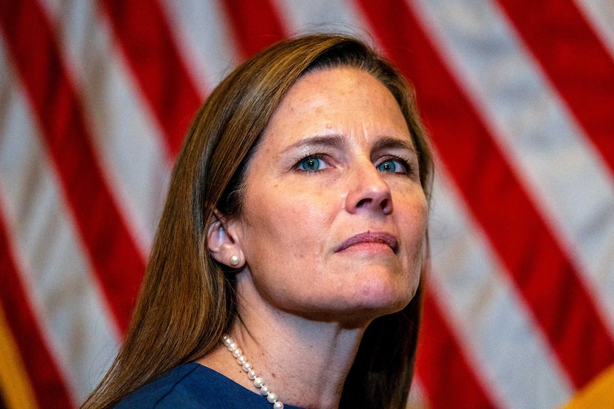 Amy Coney Barrett looking thoughtful in front of an American flag