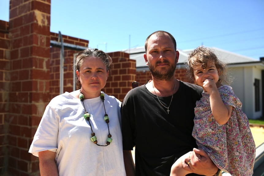 A couple and their young daughter in front of a house being built.