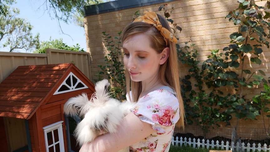 WA pet owner Kylie Board is standing in her backyard holding a fluffy rabbit