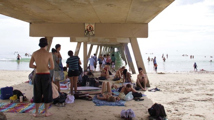 Beach-goers huddle under a jetty