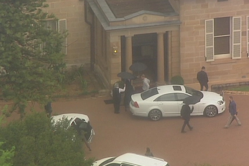aerial view of people with umbrellas welcoming man leaving white car in front of house