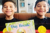 Twins Vernon and George Bond holding the children's book Day Break, smiling, wearing Aboriginal flag t-shirts.