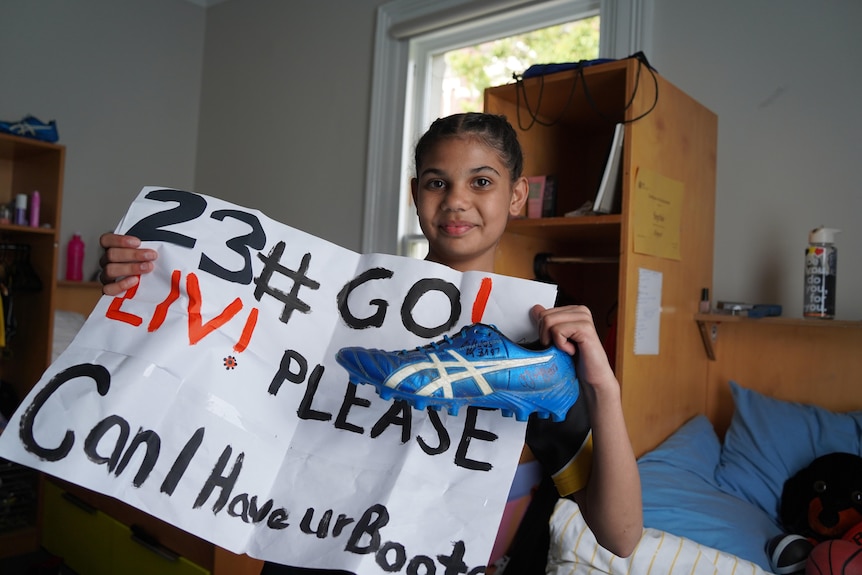 Sophie holds a footy boot and a handpainted sign saying "Liv can I have your boot"
