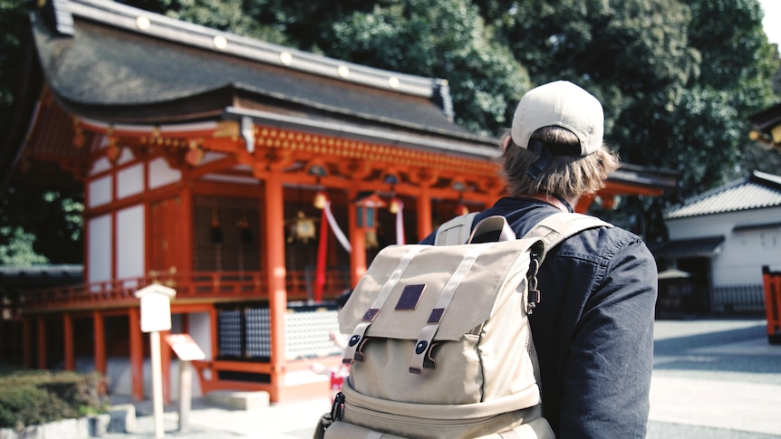 A man wearing a backpack looks at a building at the Fushimi Inari shrine in Kyoto.