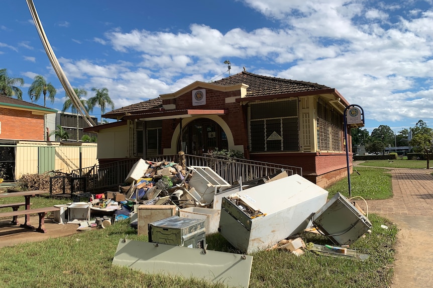 Rubbish and white goods piled up in front of a single storey brick building