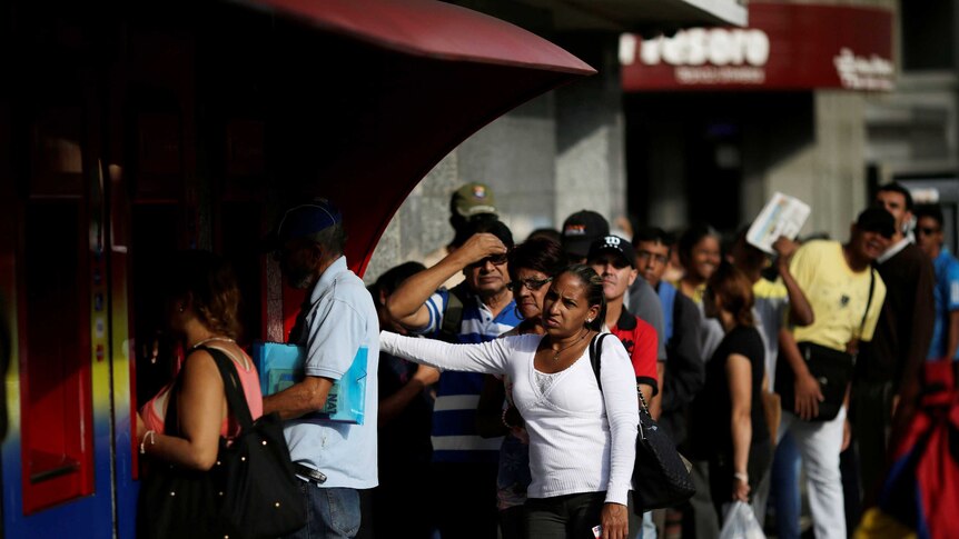 People line up to withdraw money from an automated teller in Caracas, Venezuela,