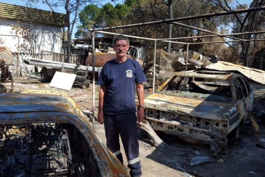 Yarloop resident Les stands among burnt out cars at the remains of his Yarloop property.