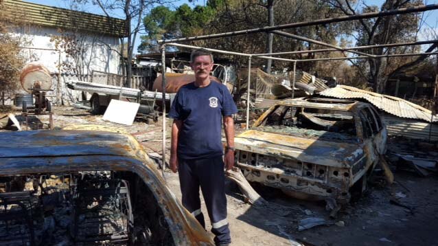 Yarloop resident Les stands among burnt out cars at the remains of his Yarloop property.