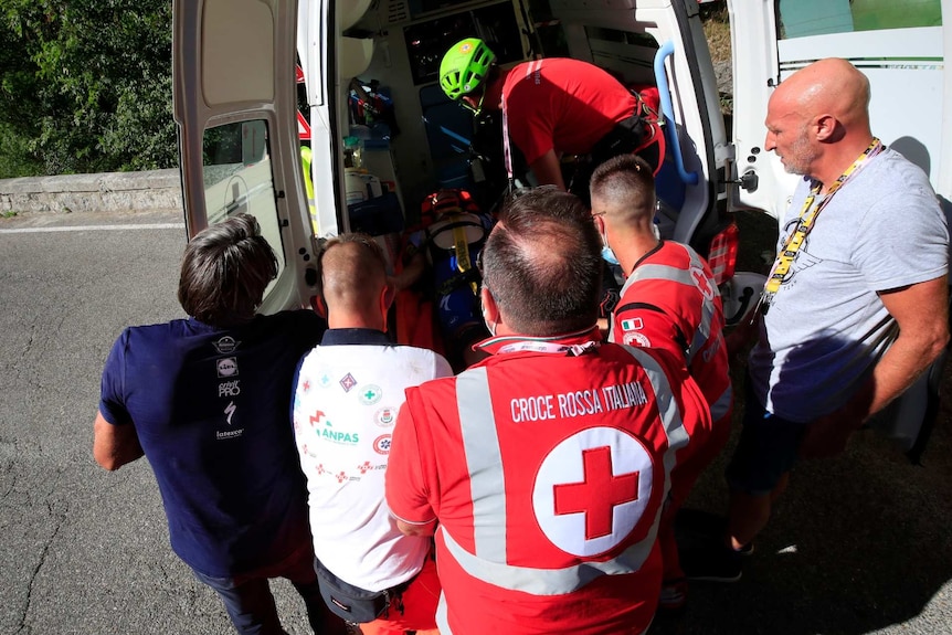 Remco Evenepoel is loaded into the back of an ambulance by medical workers as other people stand by