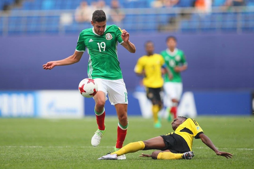 A Vanuatu footballer slips as he tackles a Mexico opponent.