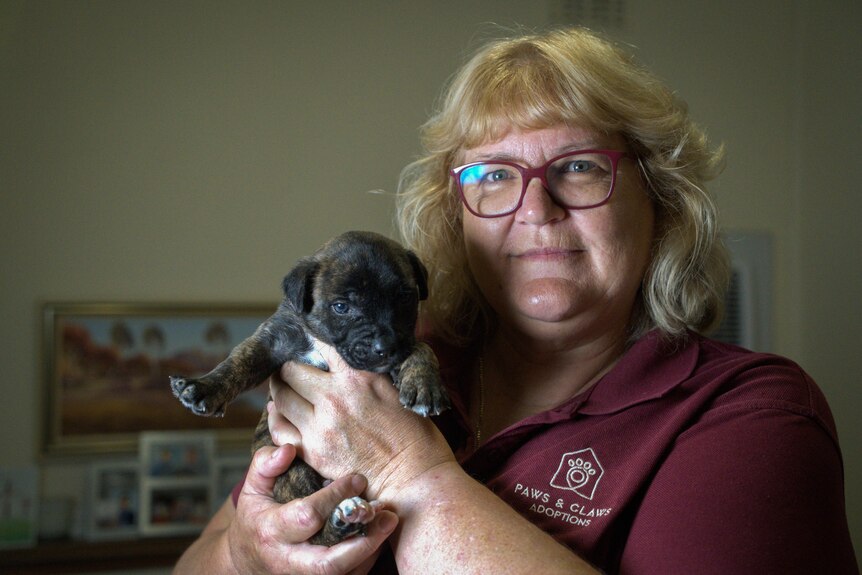 A blonde woman with glasses smiles as she holds a puppy to her face