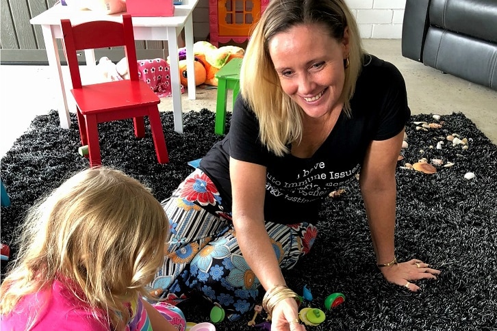 A woman plays on a mat with young children.