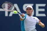 An Australian tennis player gets his racquet over on top of the ball to hit a forehand return.