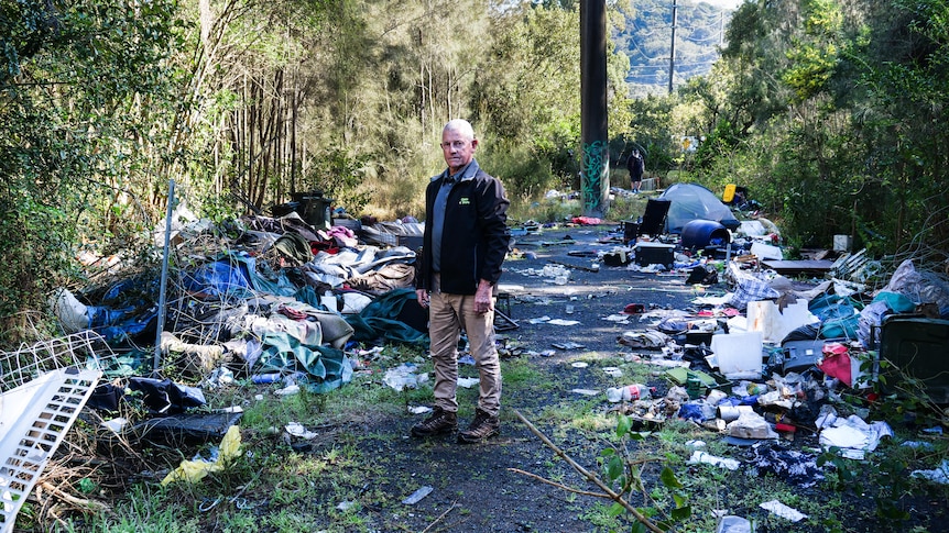 A man standing among piles of rubbish in the bush.