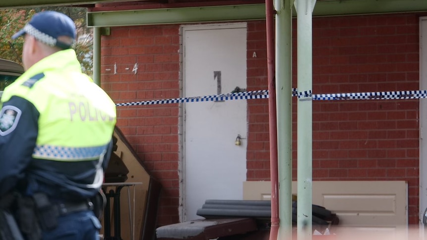 The worn front door of an apartment residence is marked off with police tape.