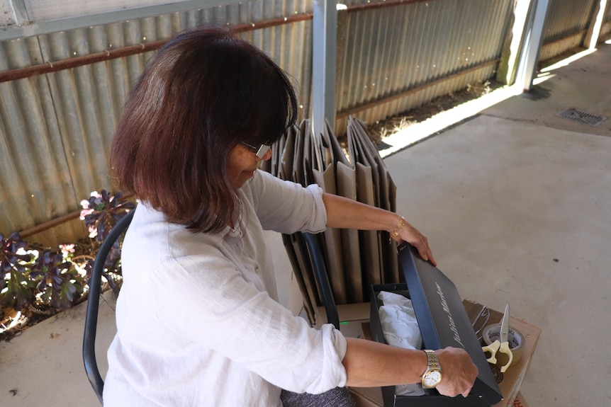 Woman in a white shirt is sitting down and looking at what's inside a shoe box.