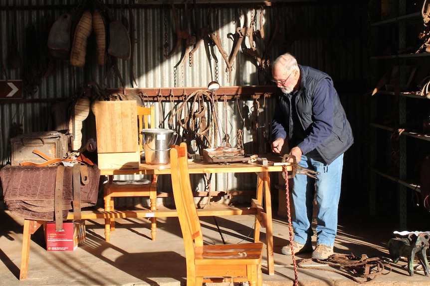 Man standing in a workshop cutting a piece of leather.