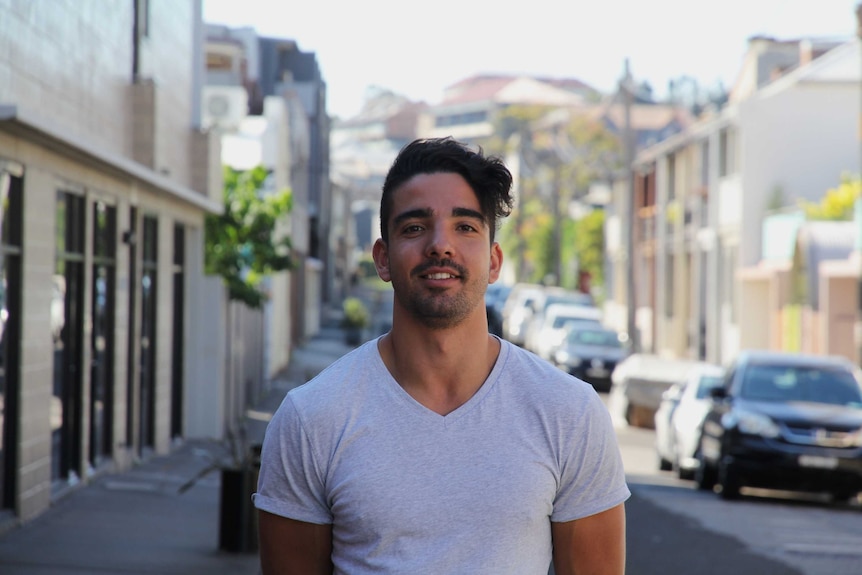 A young man in a grey t-shirt standing outside rental accommodation