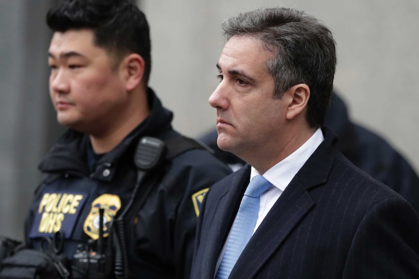 Michael Cohen leaves federal court after his sentencing next to a police officer