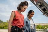 A film still of Margaret Qualley and Geraldine Viswanathan. They're looking down into the boot of a car, with confused looks.