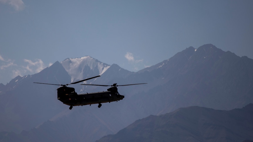 Indian air force helicopter flies in front of snow-capped mountains