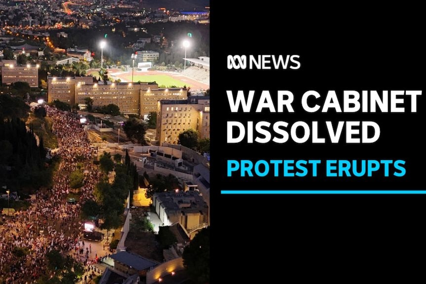 War Cabinet Dissolved, Protest Erupts: Aerial shot of a city at night with crowds of people on a main street.
